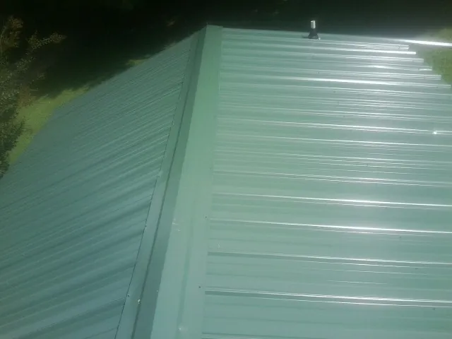 New green metal panels meeting at the ridge of a roof — Flat Roof Repair work by our crew in Hamer