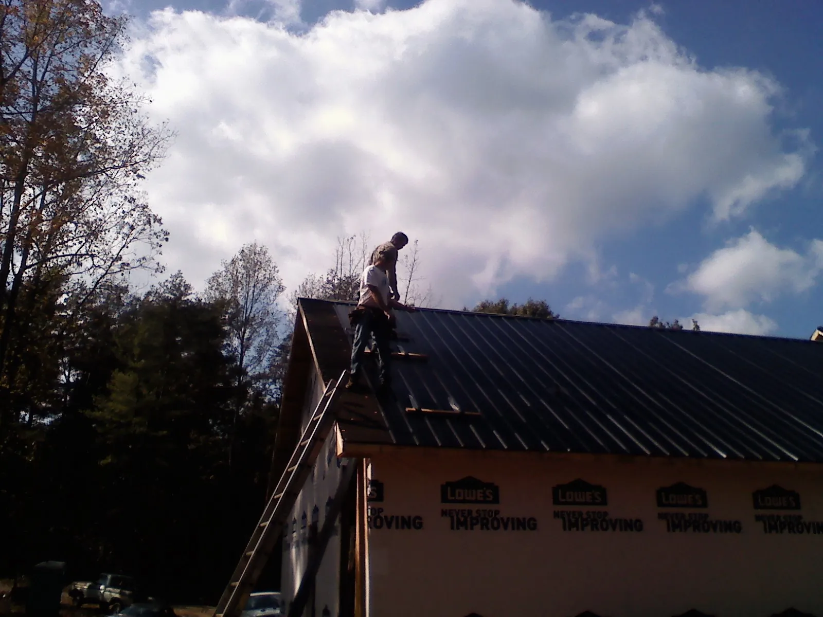 Roofer fastening dark metal panels high against a cloudy sky, from a Roof Inspection job in Hamer